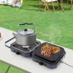 Portable camping stove heating a kettle and grilling steaks at a campsite.